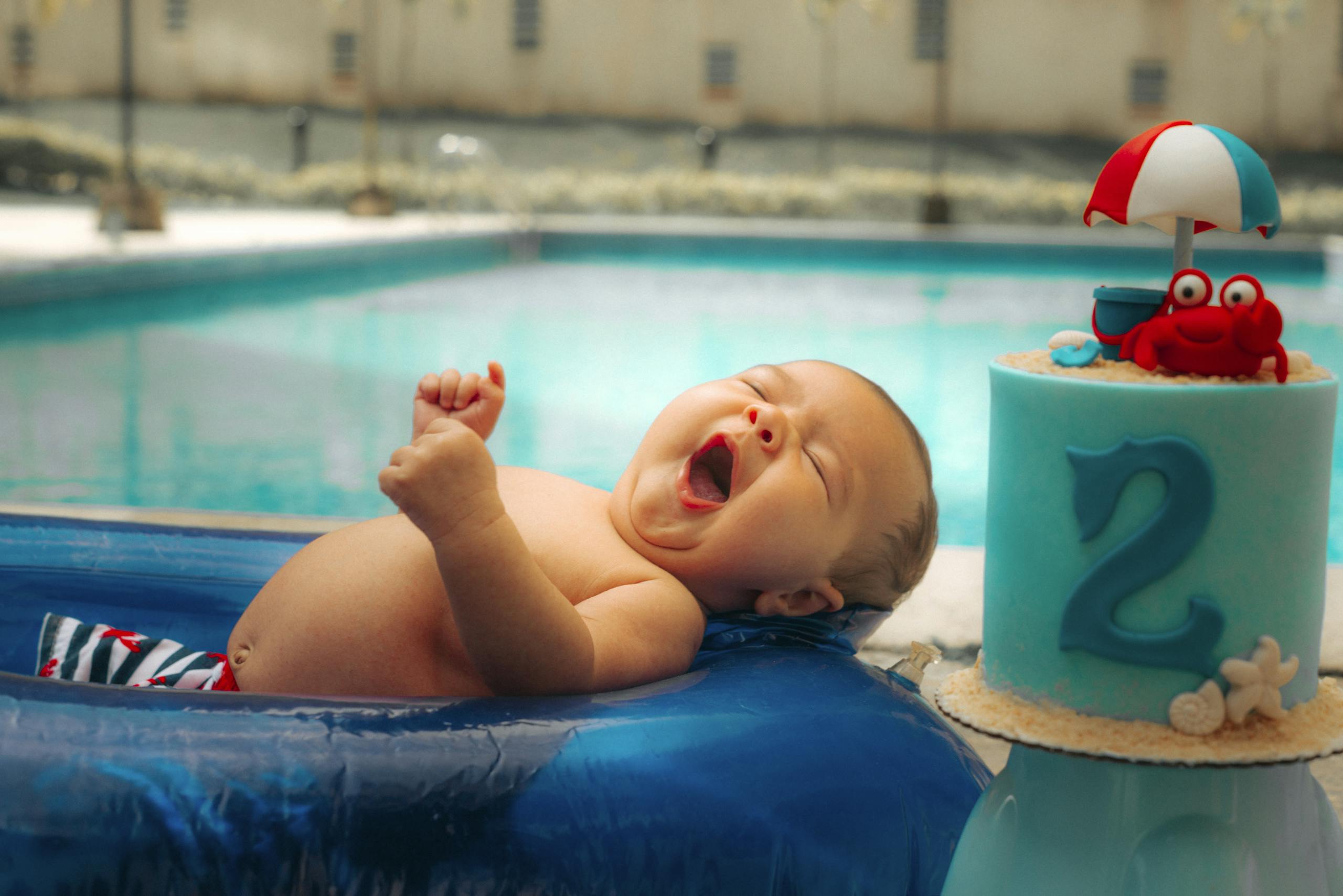 Cute baby enjoying a sunny day by the blue pool with a colorful cake. Perfect summer vibe.