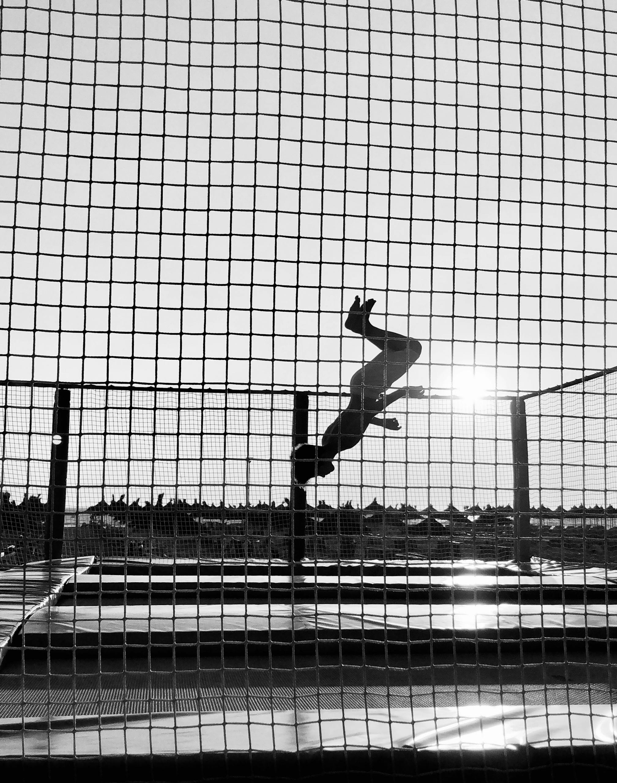 Silhouette of a person mid-flip on a trampoline against sunlight in urban area, Durrës, Albania.