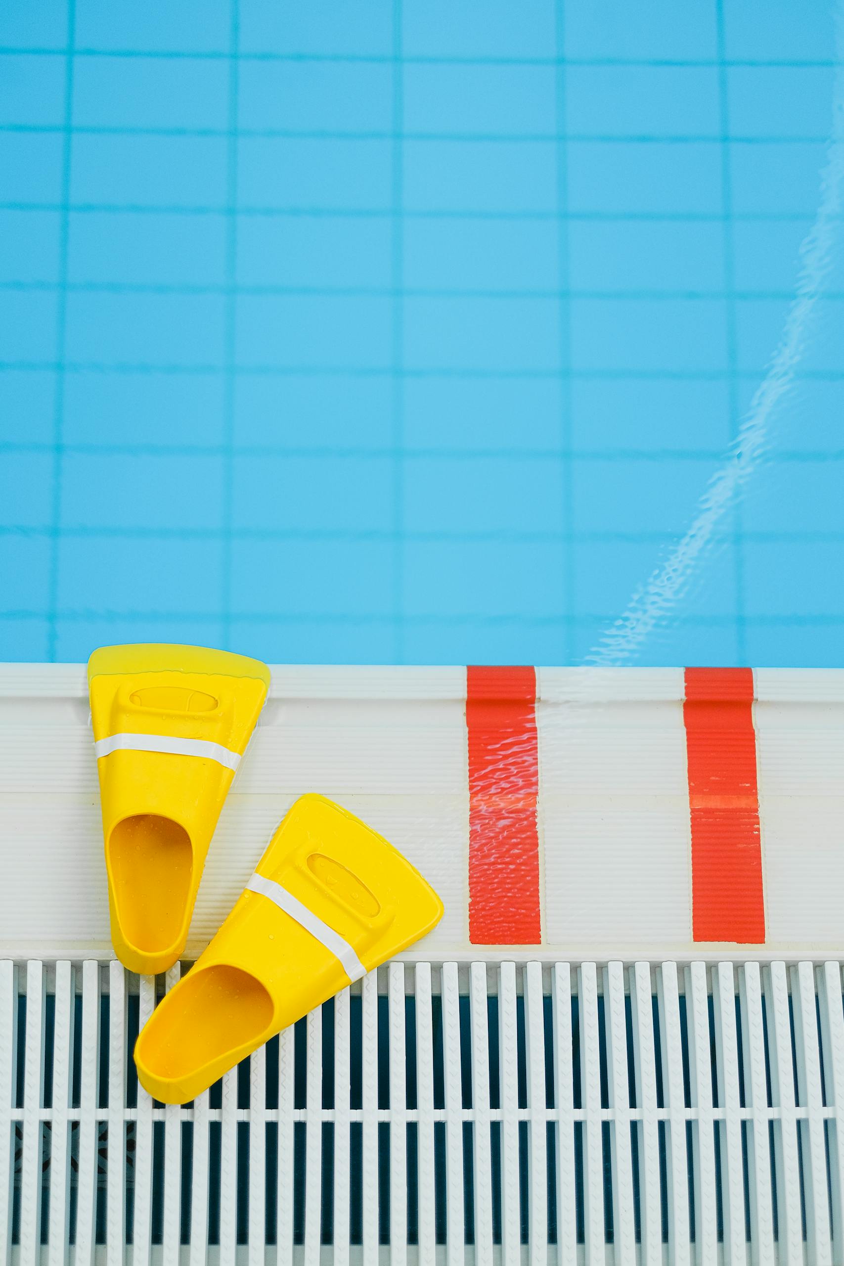 Yellow flippers placed at the edge of a vibrant blue swimming pool, ready for aquatic activities